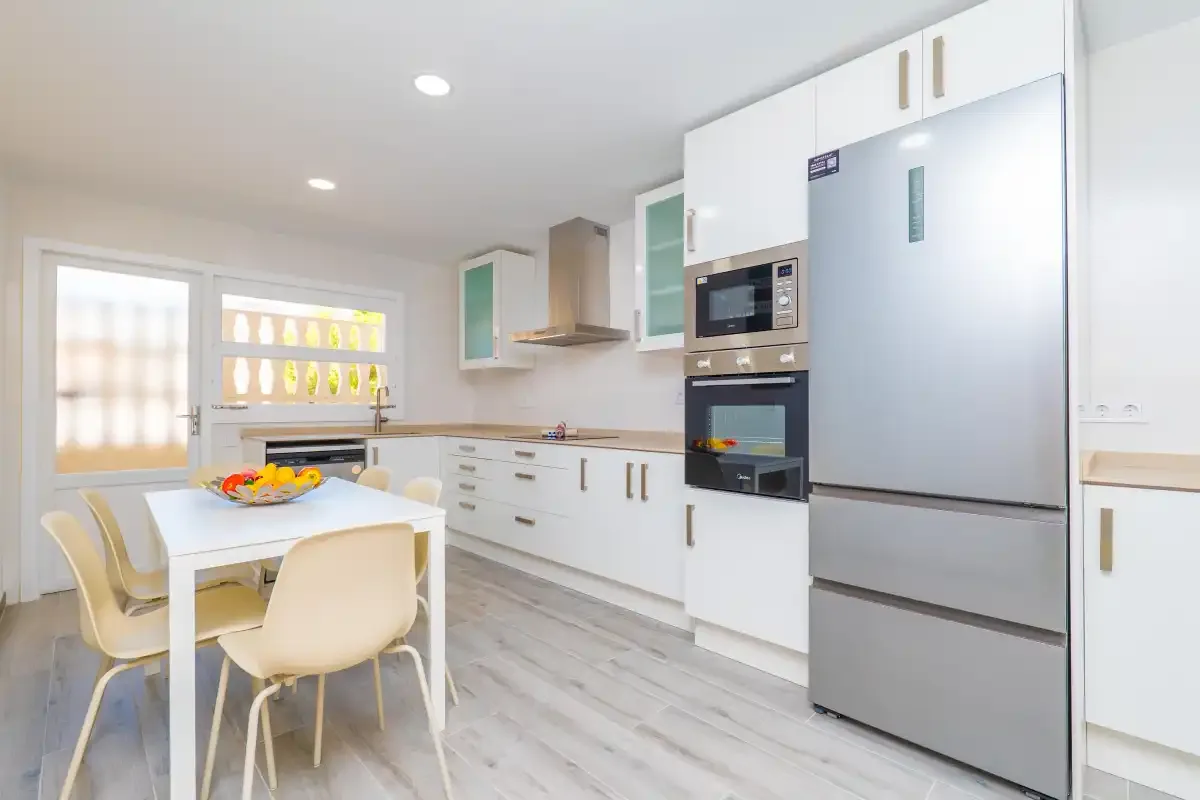 Una cocina luminosa con zona de comedor, armarios blancos y una mesa.