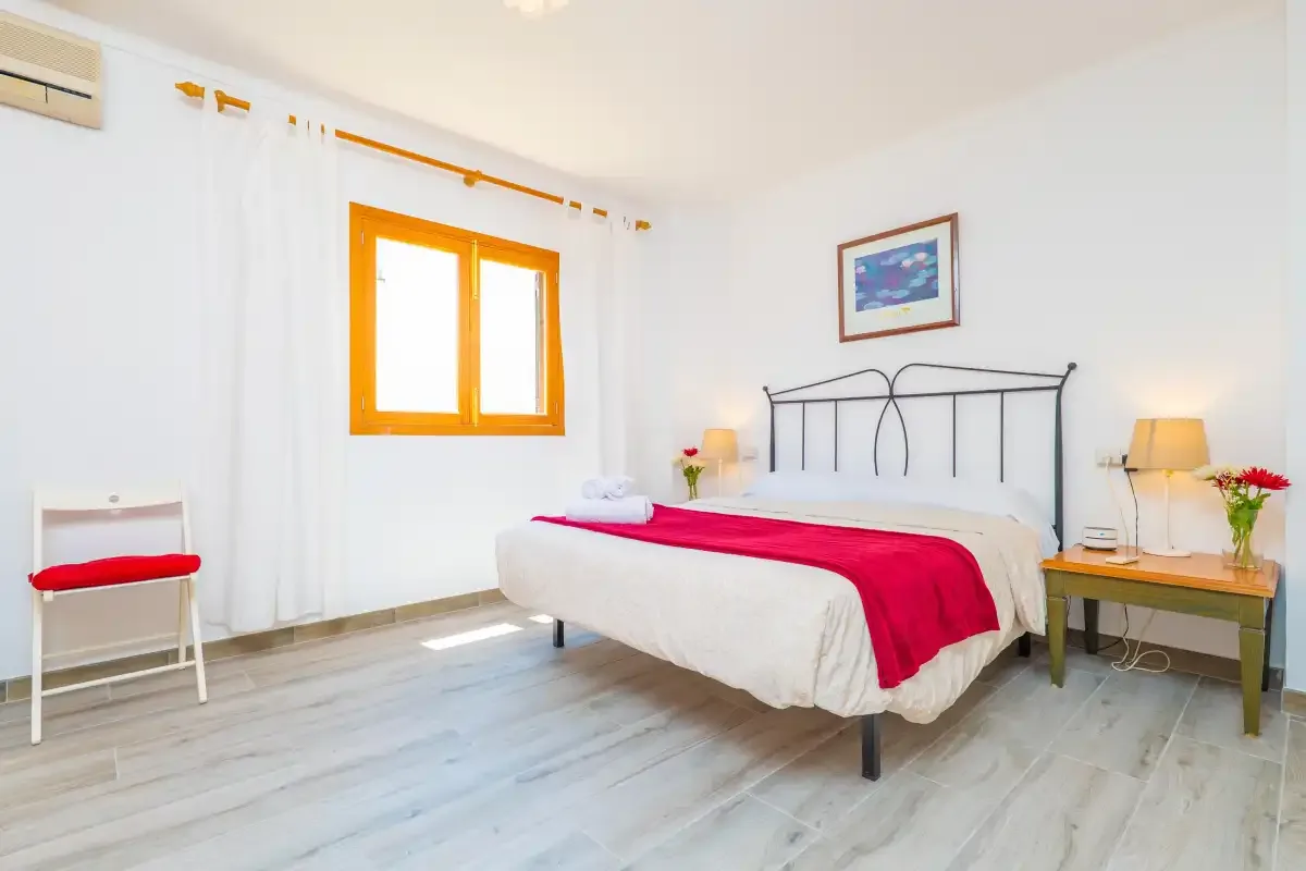 Un dormitorio luminoso con una cama doble y una colcha roja.
