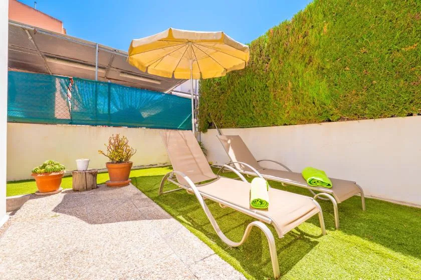 Un patio soleado con tumbonas reclinables, una sombrilla amarilla y plantas en macetas.