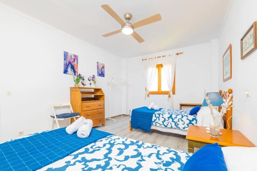 Un dormitorio luminoso con camas, ropa de cama azul estampada y una ventana soleada.