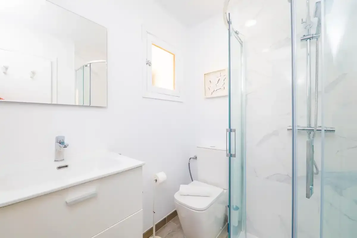 Un baño luminoso con lavabo, inodoro y ducha de cristal.