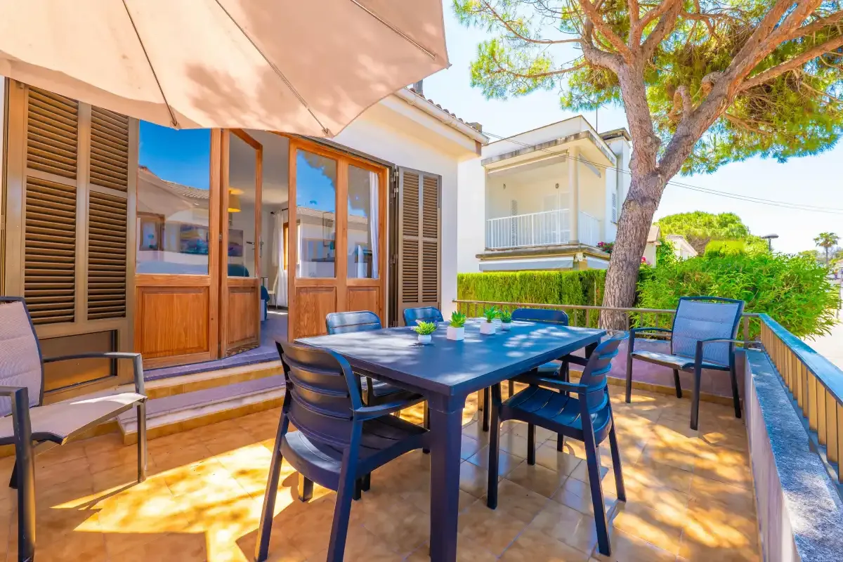 Un comedor en el patio con una mesa y asientos junto a la casa.