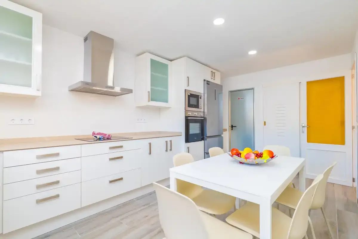 Una cocina luminosa y moderna con armarios blancos y una mesa de comedor.