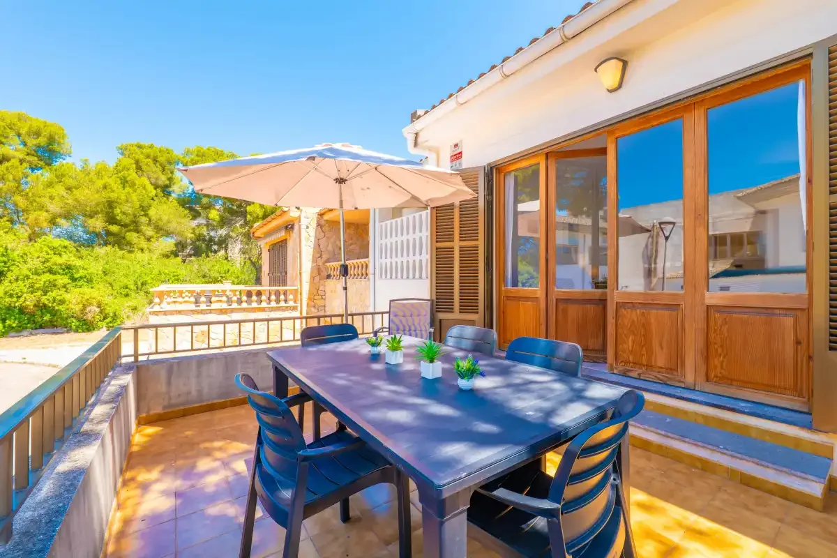 Una zona de comedor al aire libre con mesa, asientos y una sombrilla.