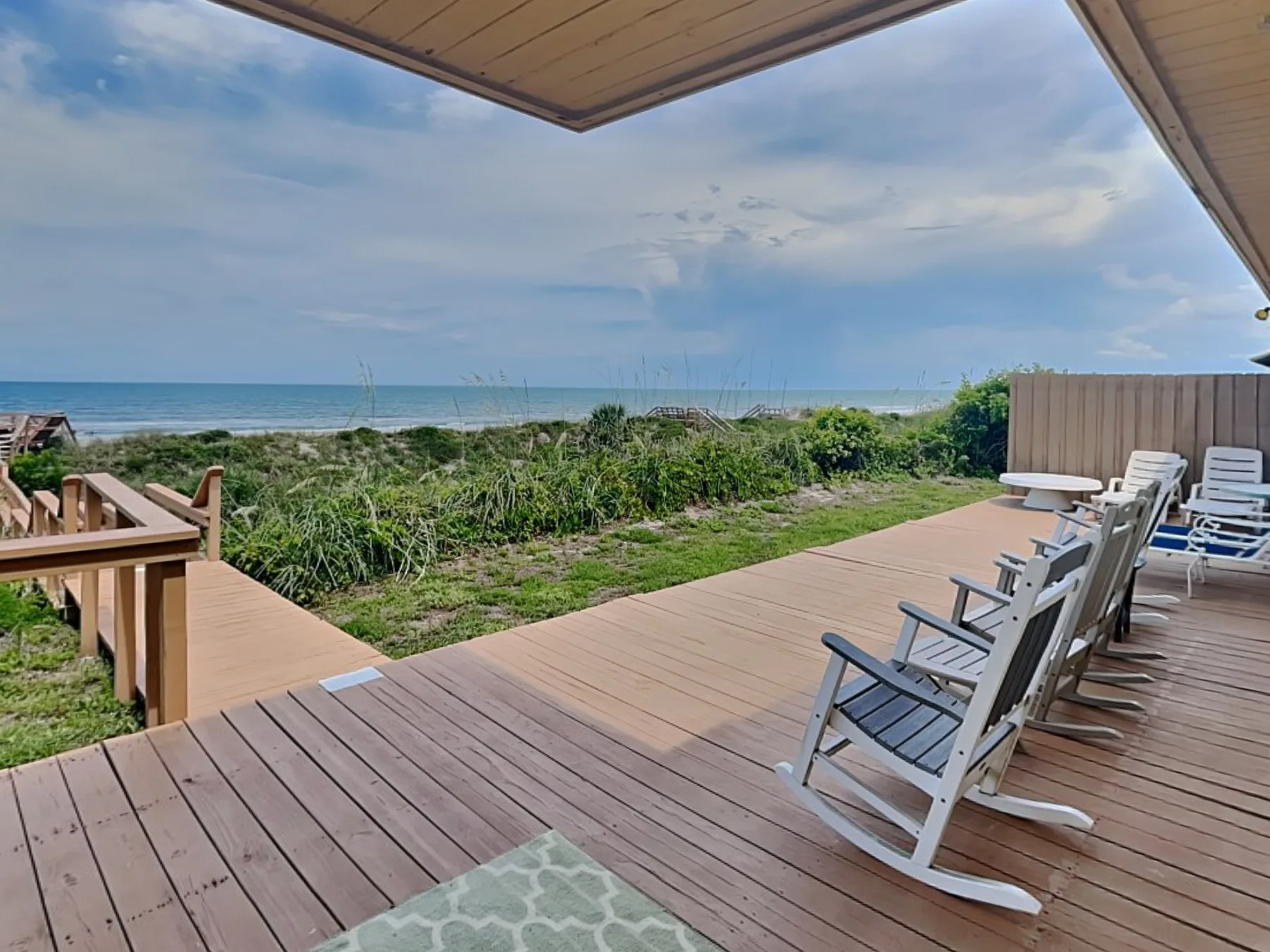 A seaside deck with outdoor seating overlooks coastal vegetation and the ocean.