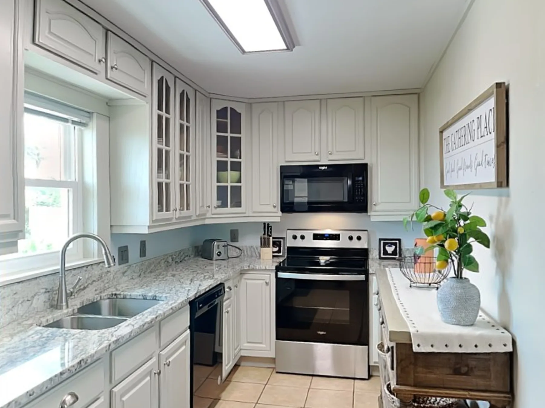 A bright kitchen with white cabinetry, a stone countertop, and stainless steel appliances.