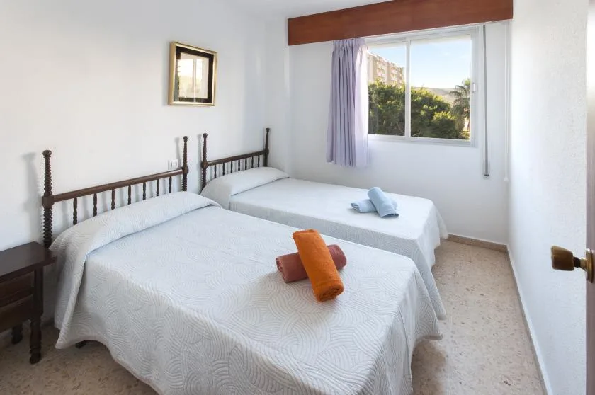 Un dormitorio luminoso con dos camas y una ventana con vistas a la vegetación.