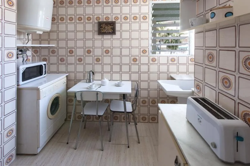 Una cocina alicatada con una mesa y electrodomésticos junto a una ventana.