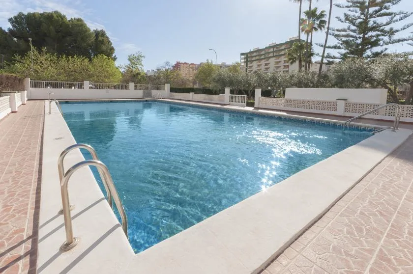 An outdoor swimming pool is surrounded by paved decking and a low fence.
