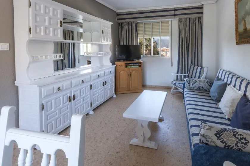 Una sala de estar con asientos a rayas, una mesa de centro blanca y un televisor.