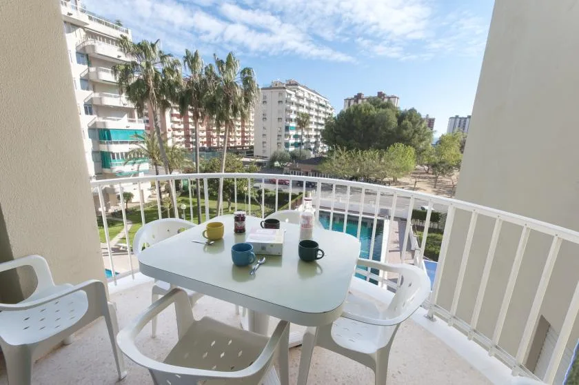 A balcony dining area overlooks a pool, palm trees, and nearby apartment buildings.