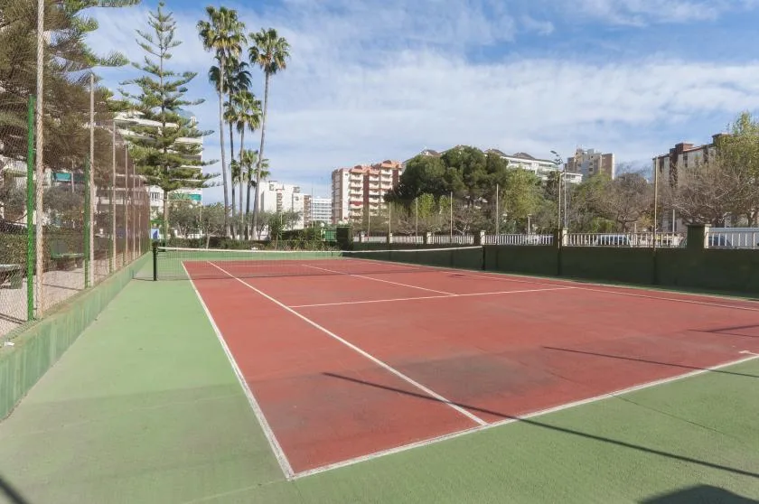 Una cancha de tenis al aire libre con superficie roja y perímetro verde.