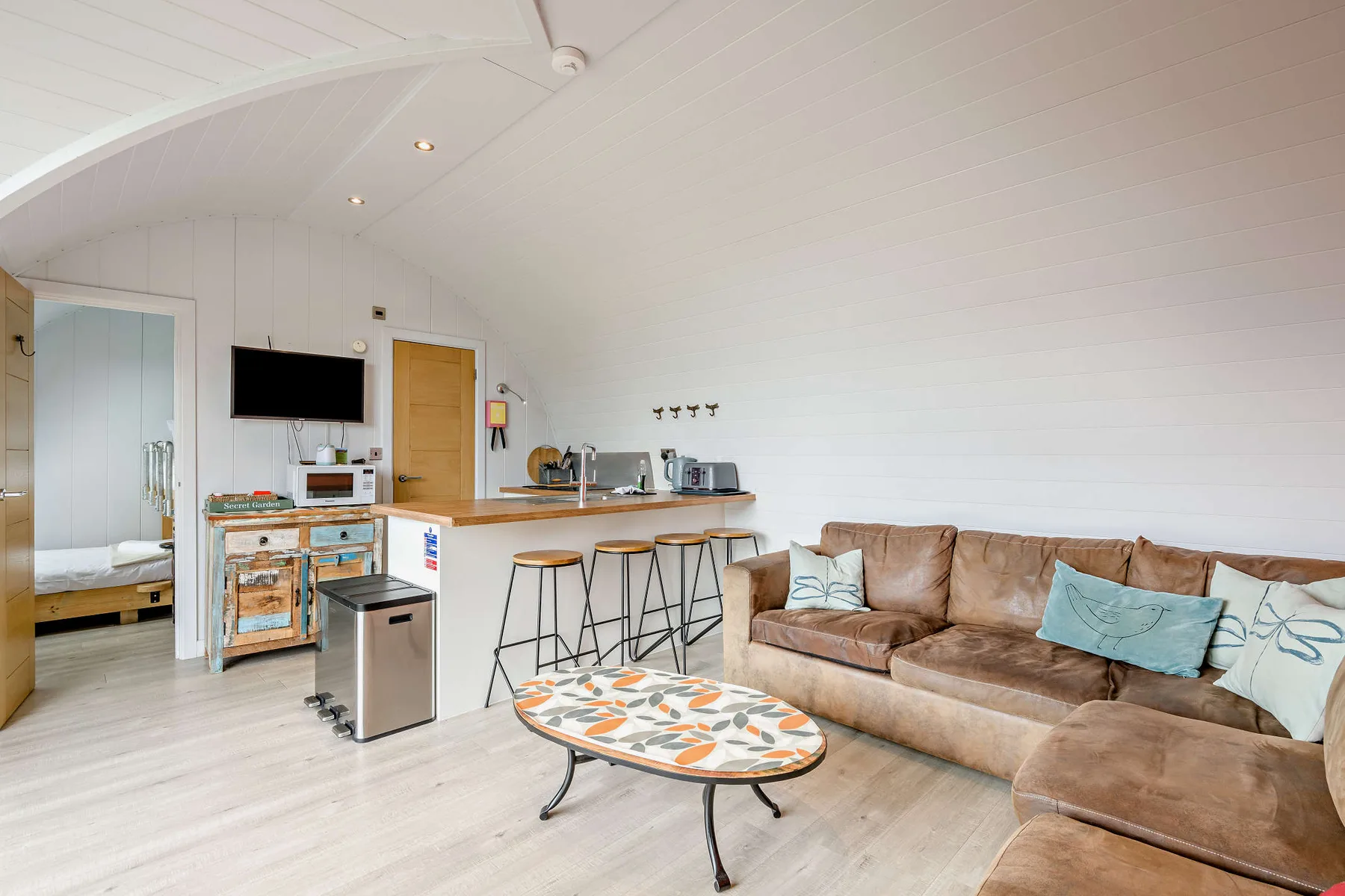 Open-plan living area with a brown sectional, coffee table, and compact kitchen.