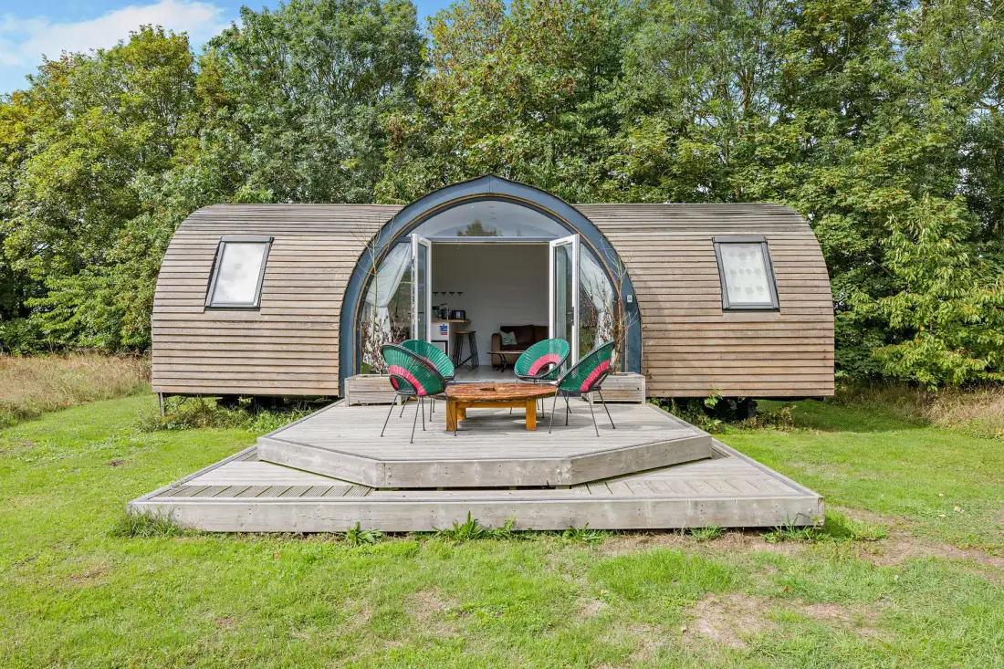A wooden cabin with a curved central entrance and a raised outdoor deck.