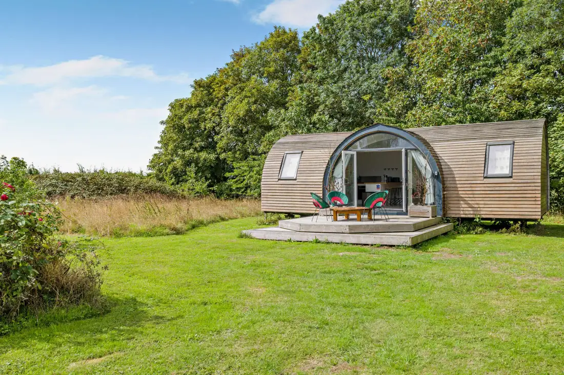 A small wooden cabin sits on a grassy lawn beside trees.
