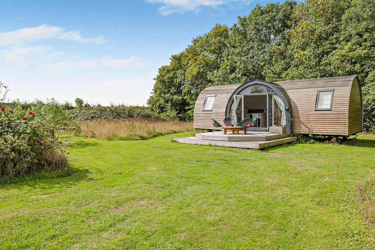A curved wooden cabin opens onto a grassy garden.