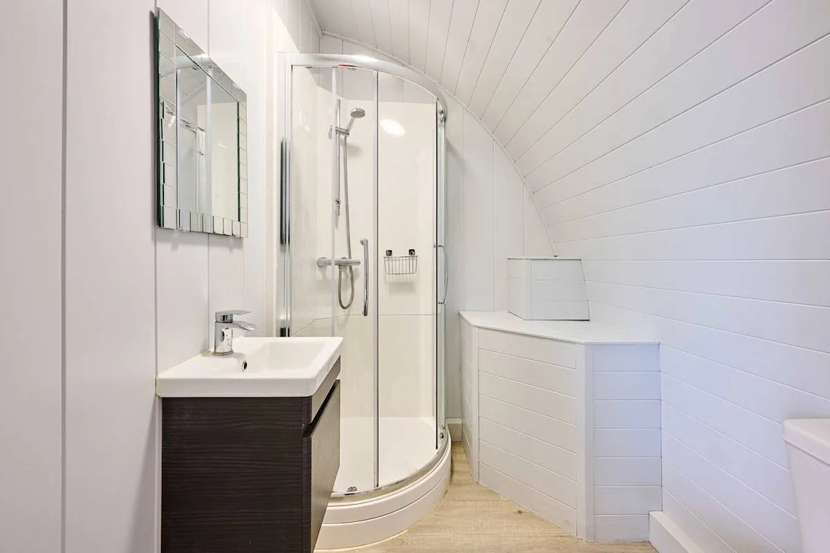 A bright bathroom with a shower and sink beneath a sloped ceiling.