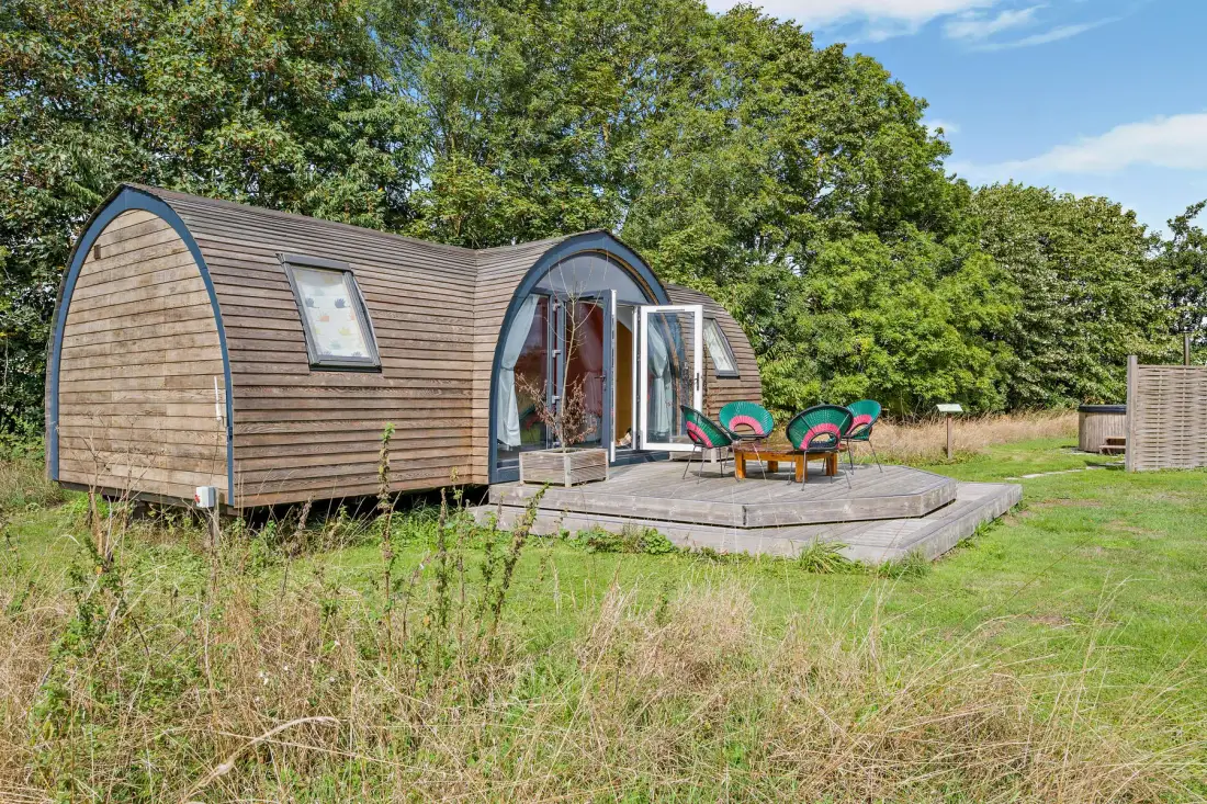 A small wooden cabin opens onto a raised deck with outdoor seating.