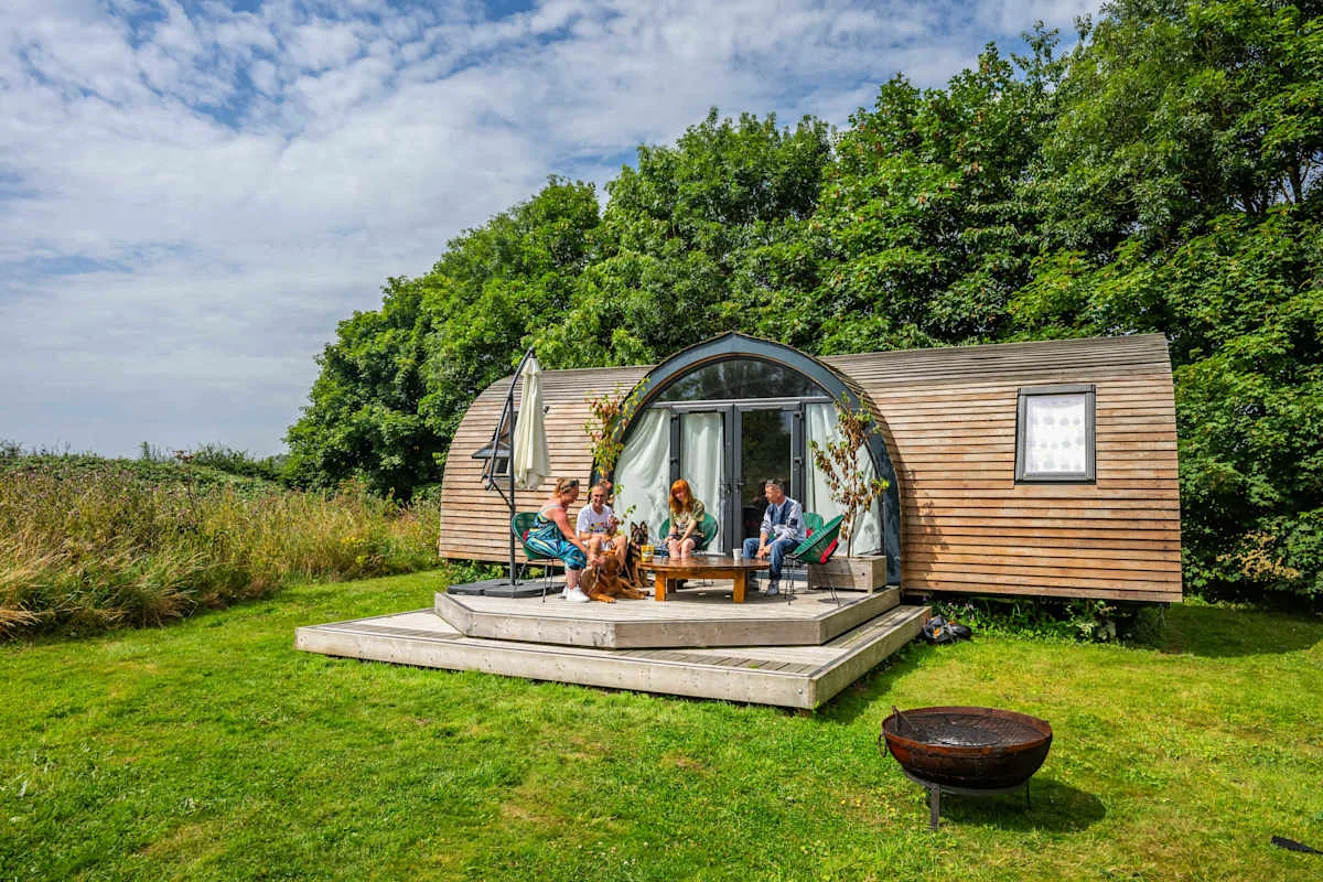 A wooden cabin with a curved glass front opens onto a grassy garden.