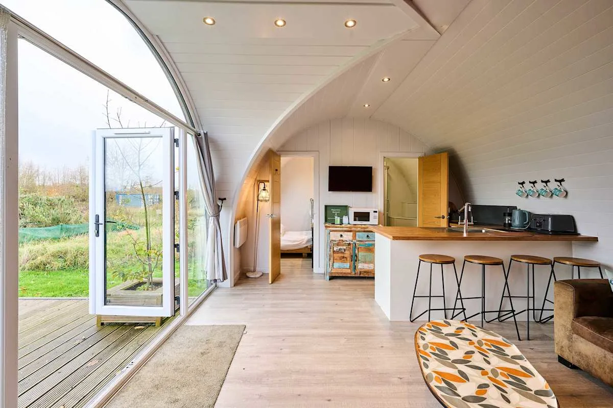 A bright open-plan living area with a kitchen, bar seating, and garden views.