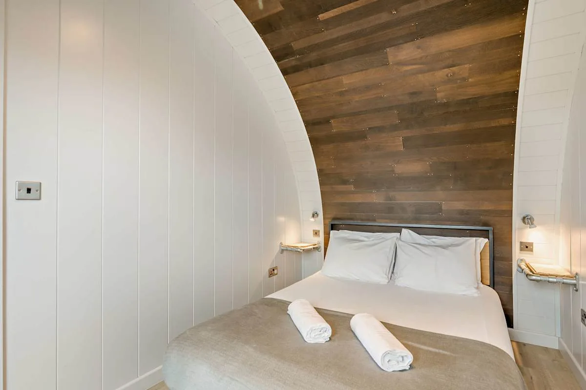 A bedroom with a bed beneath a curved ceiling and dark wood paneling.