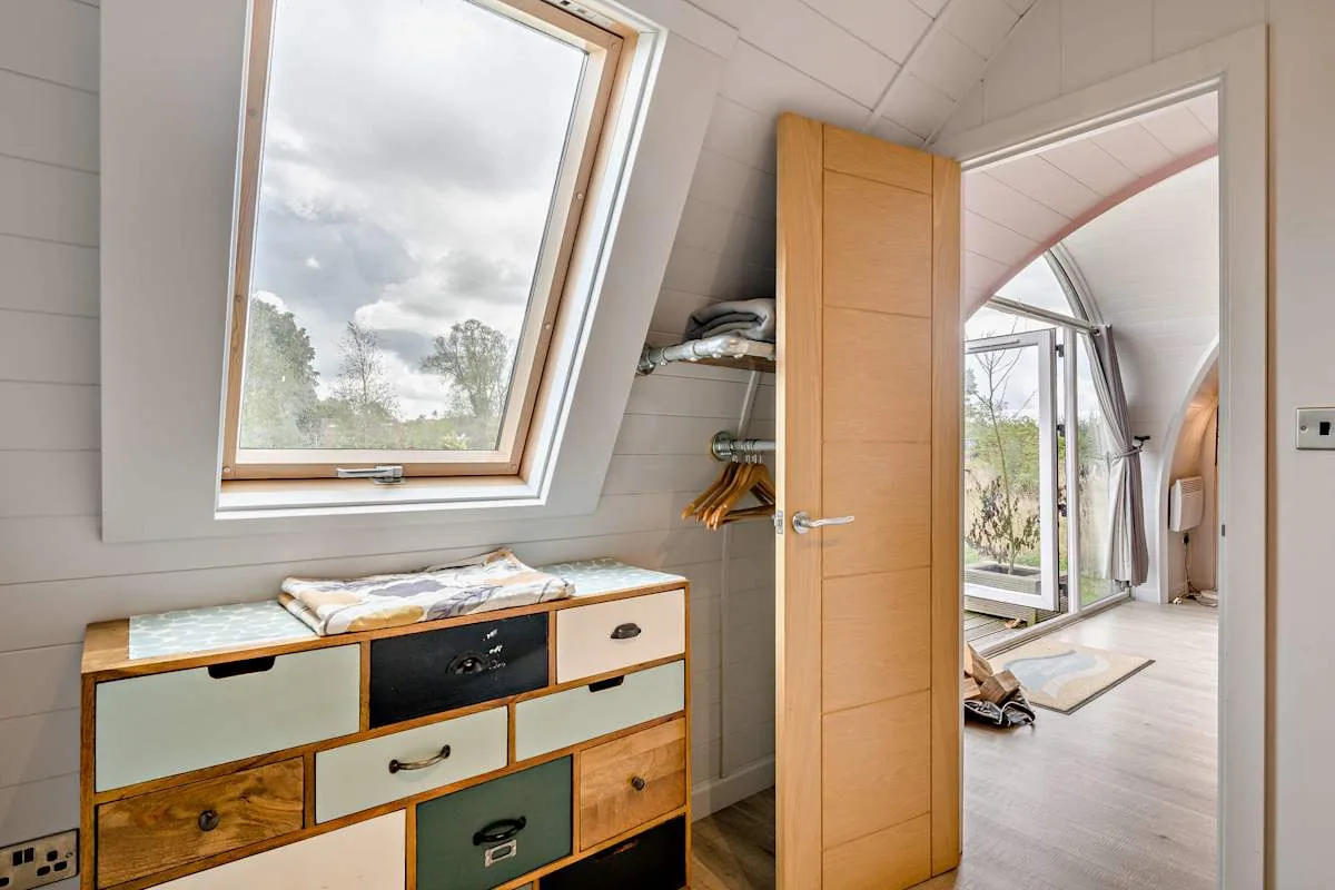 A bright attic dressing area opens through a wooden door to a glass-enclosed space.