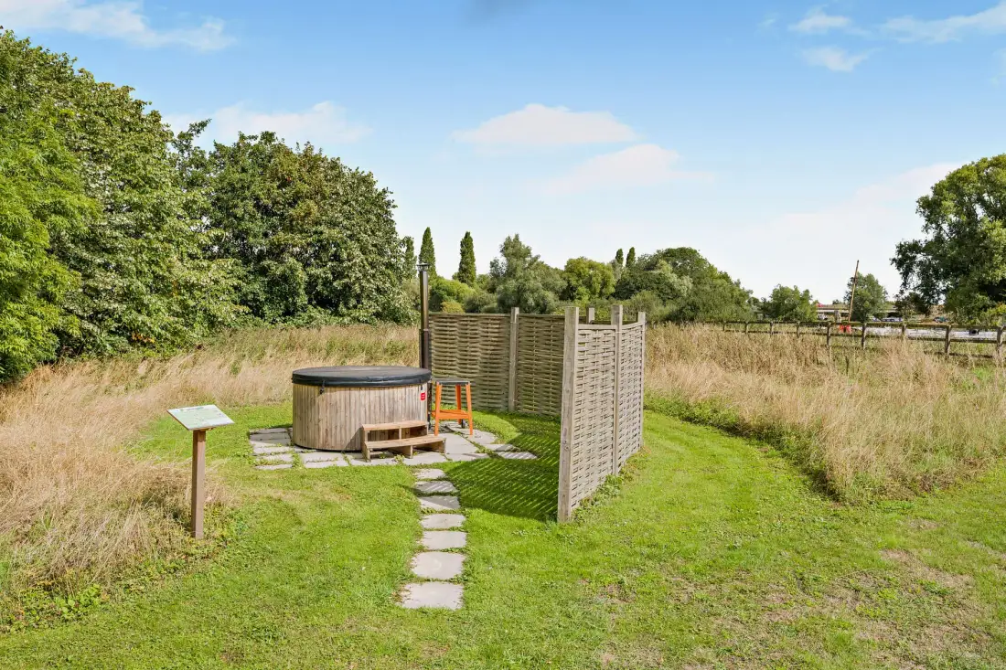An outdoor hot tub sits beside a grassy path and wooden privacy screens.