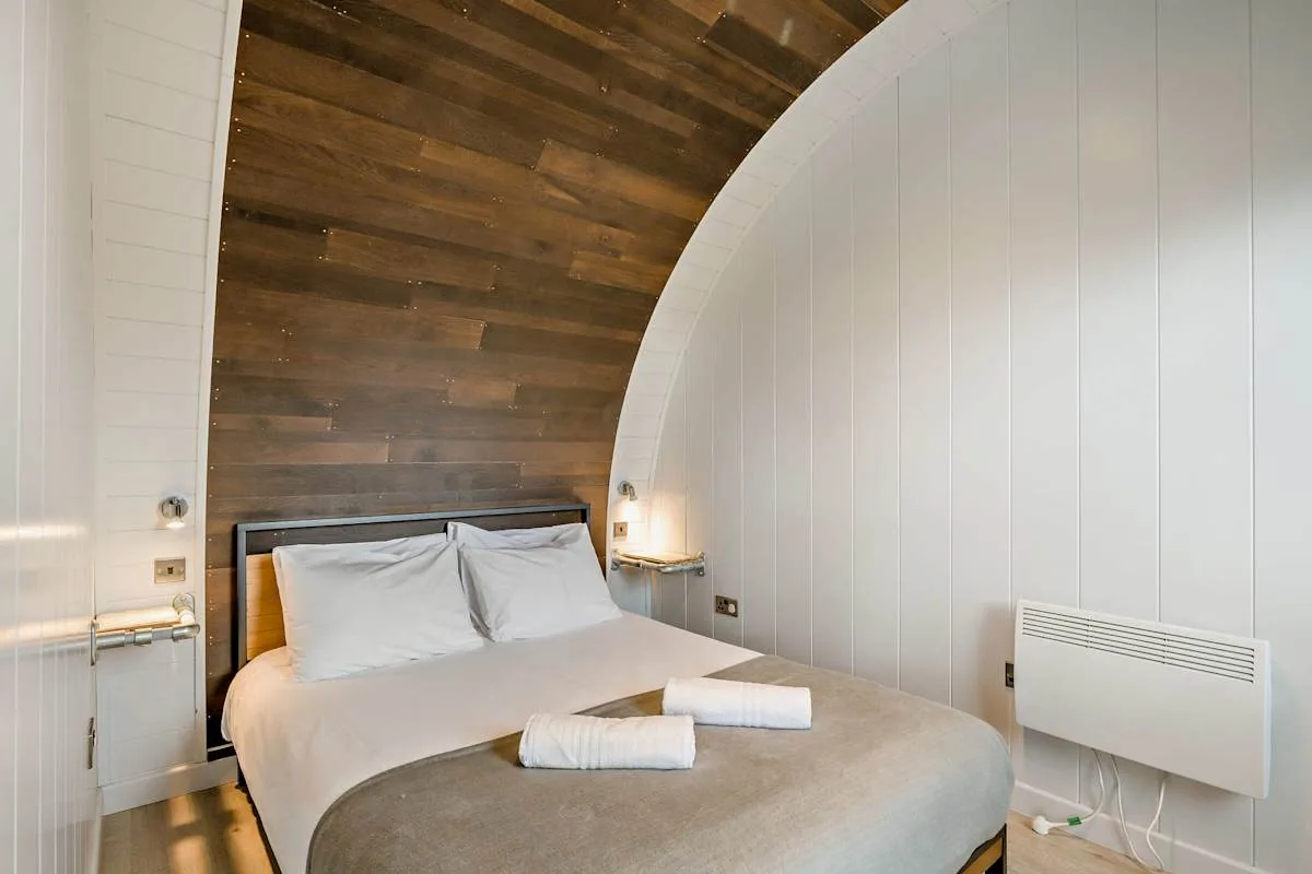 A bedroom with a bed and folded towels beneath a curved wood-paneled ceiling.