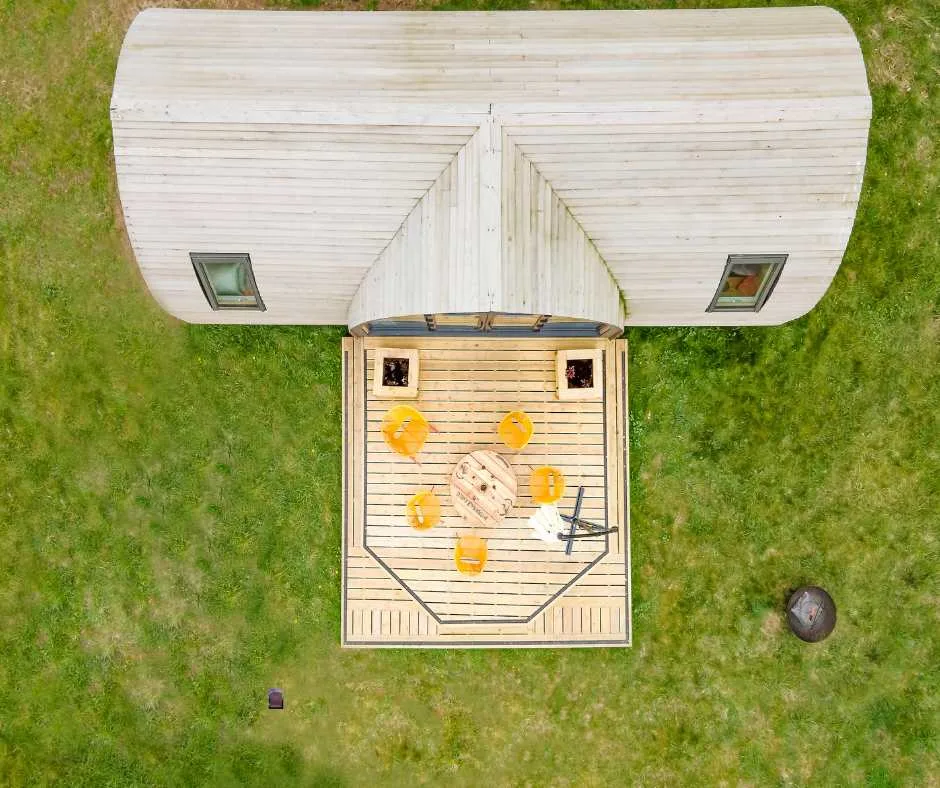 An aerial view shows a small outdoor deck beside a white cabin on grass.