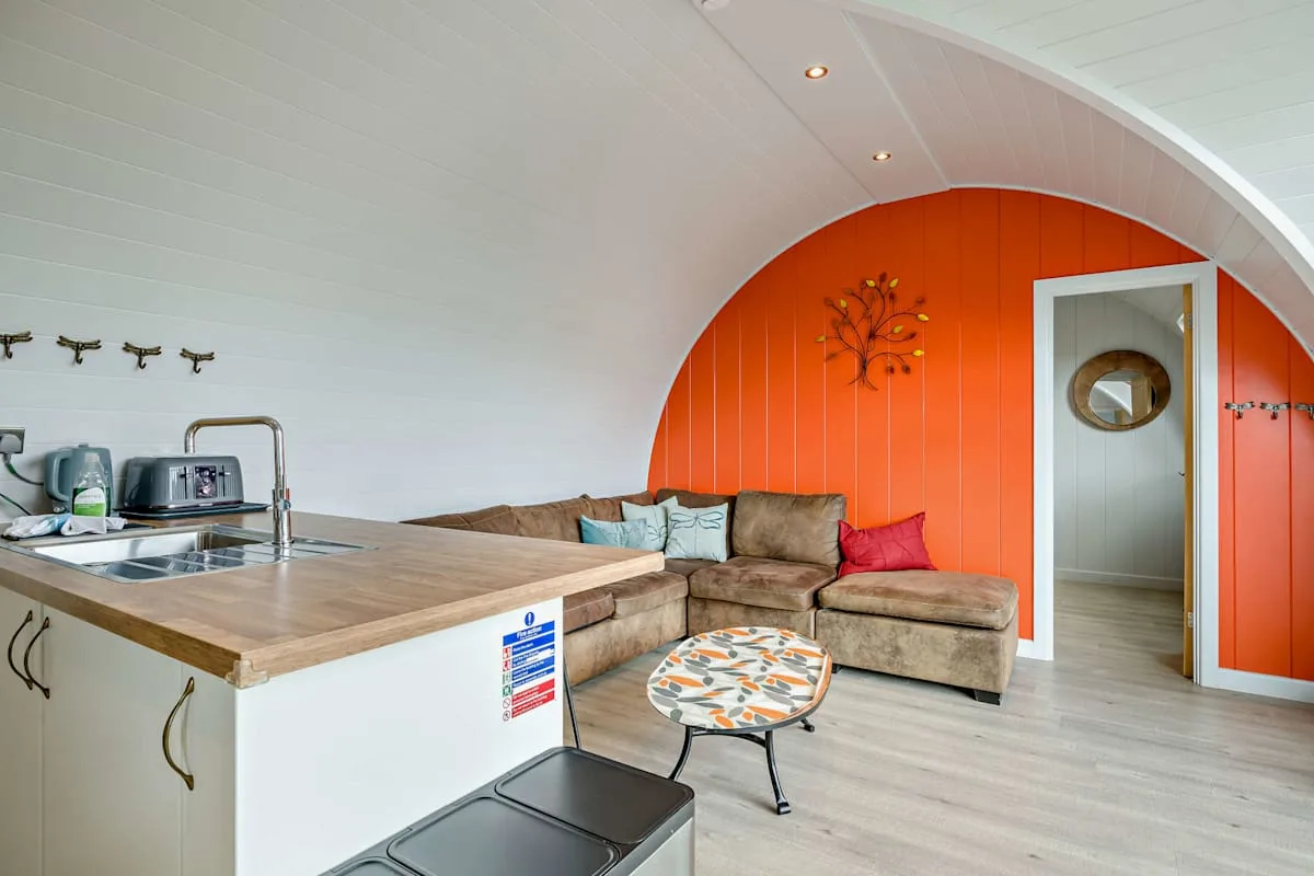 A bright lounge with a curved ceiling, colorful seating, and a small kitchenette.