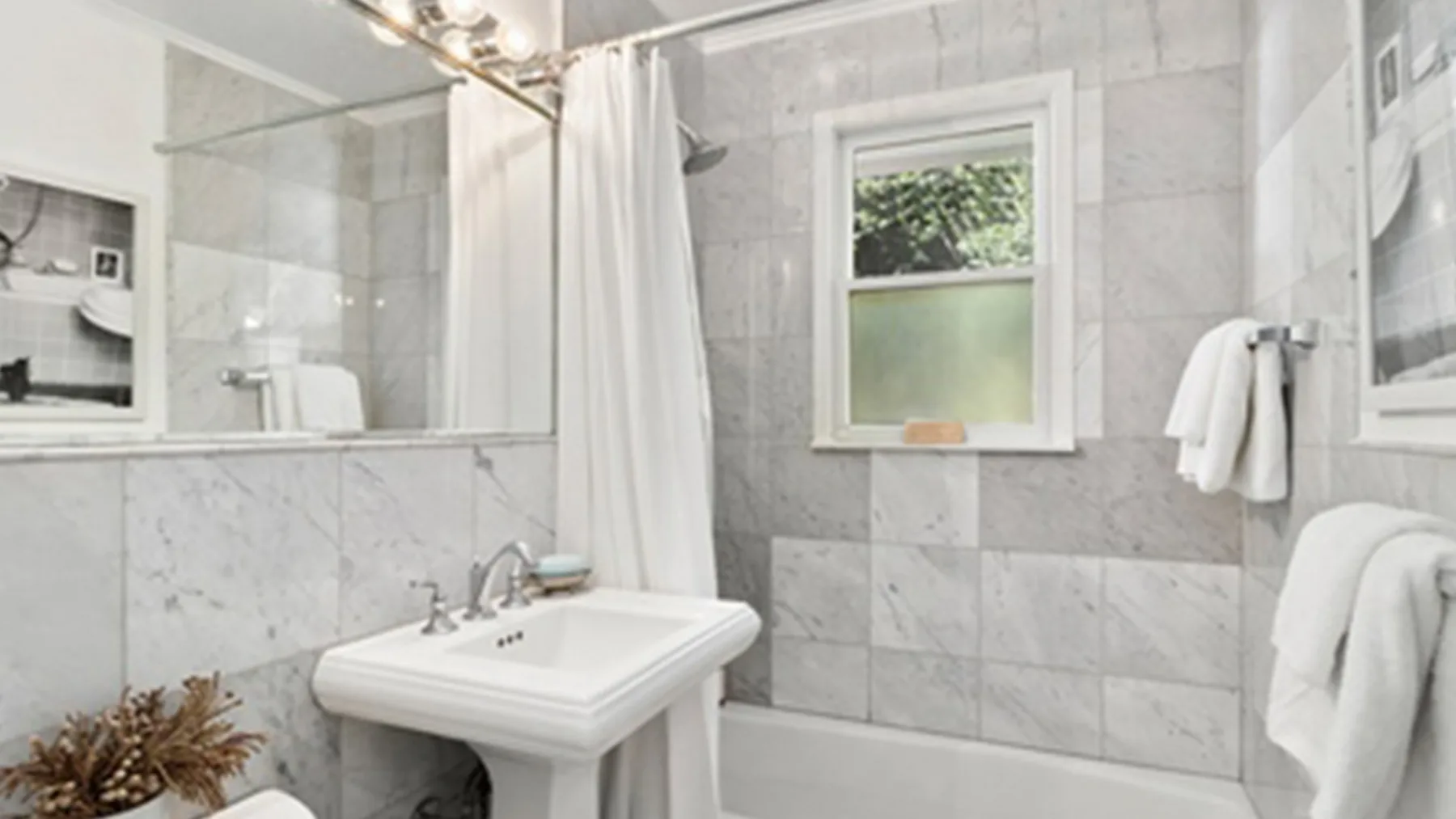 Un baño alicatado con lavabo, espejo y cortina de ducha junto a una ventana.