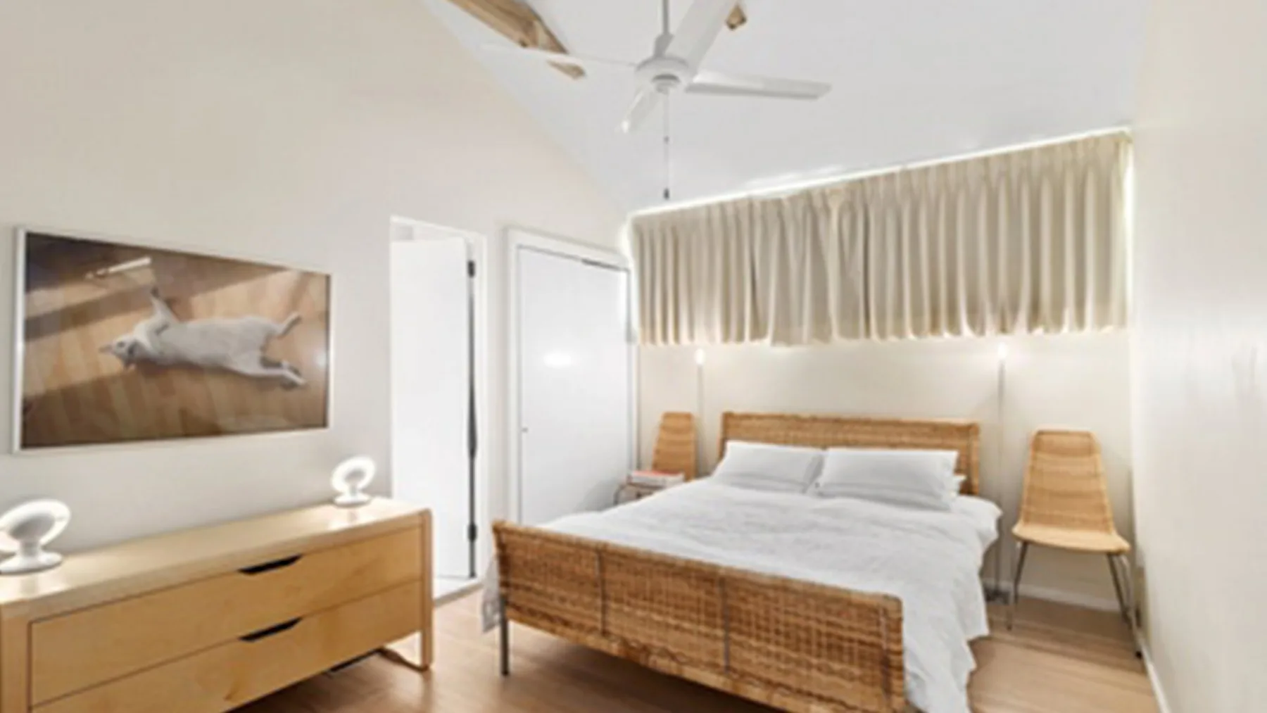 Un dormitorio con una cama, una cómoda de madera y cortinas claras.