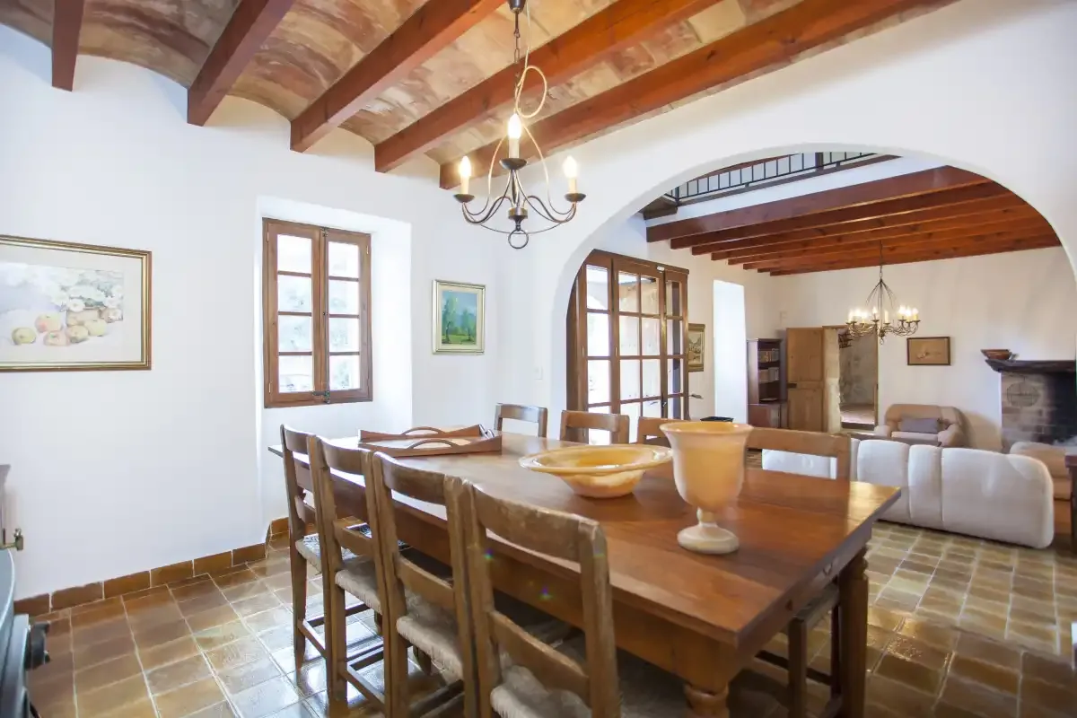 A dining room with a wooden table and seating beneath exposed ceiling beams.