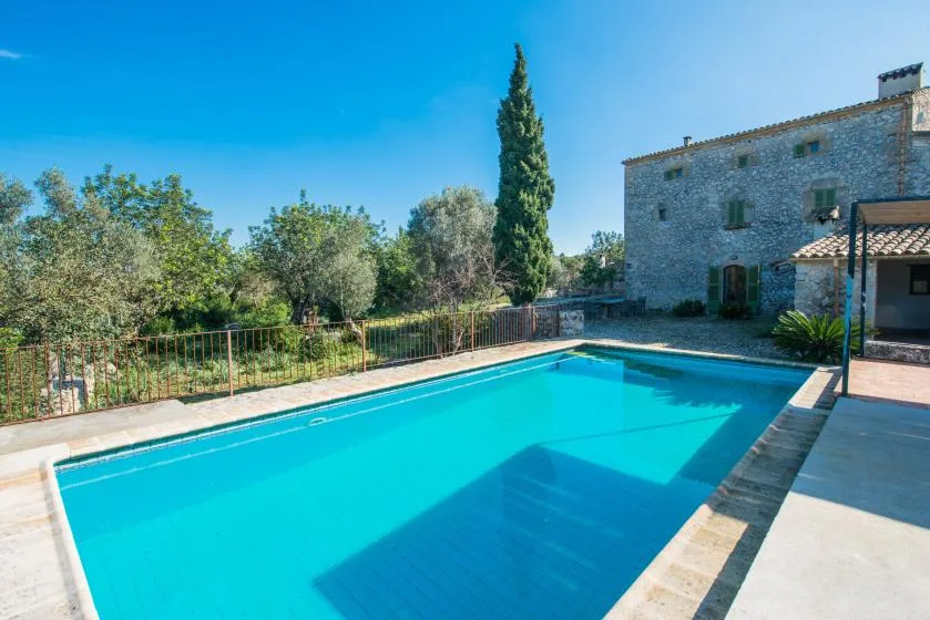 Una piscina al aire libre está junto a un edificio de piedra y un jardín.