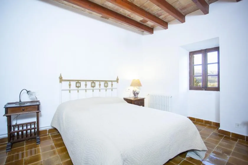 A bedroom with a bed beneath exposed wooden ceiling beams and a window.