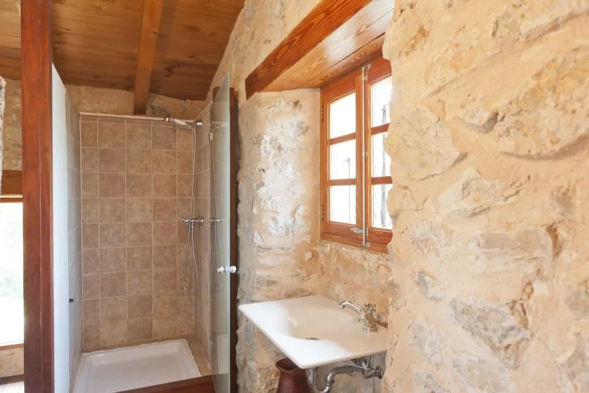 A rustic bathroom with a shower, sink, and wooden-framed window.