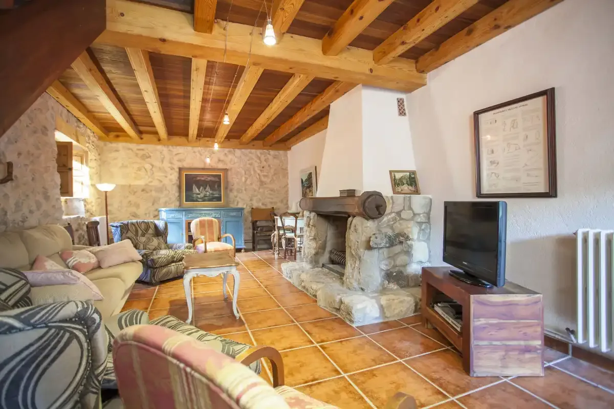 A living room with seating, a stone fireplace, and exposed wooden ceiling beams.