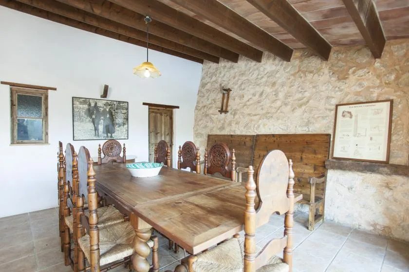 A rustic dining room with a long wooden table beneath exposed ceiling beams.