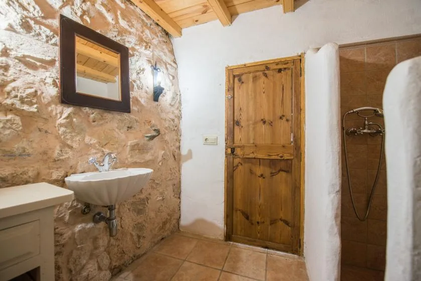 A rustic bathroom with a stone wall, wooden door, and shower.