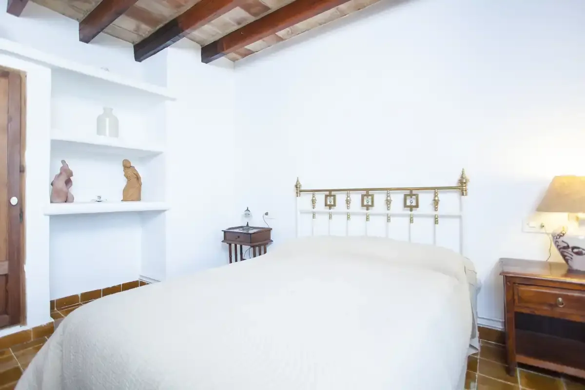 A bright bedroom with a white bed beneath exposed wooden ceiling beams.