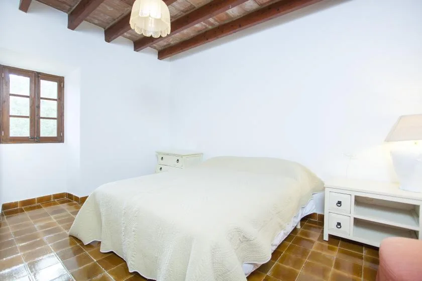 A bedroom with a bed beneath exposed wooden ceiling beams.