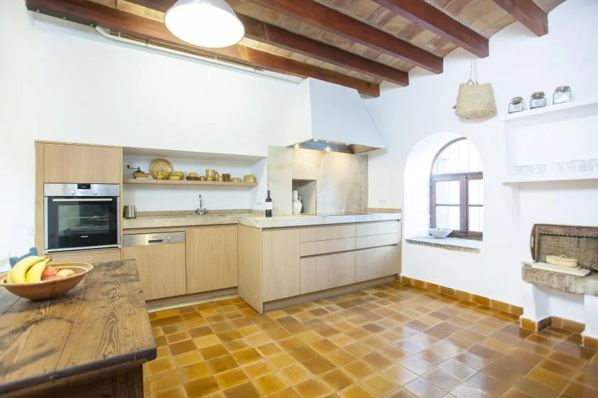 A bright kitchen with wooden cabinetry, a tiled floor, and exposed ceiling beams.
