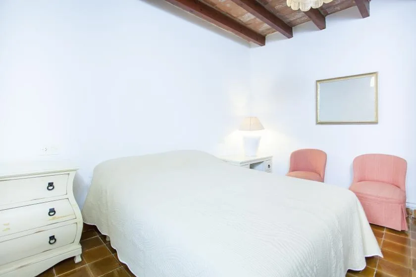 A bedroom with a bed, two chairs, and a bedside table.