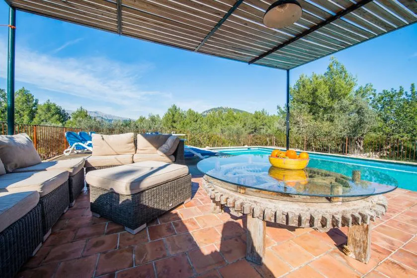 Una zona de estar exterior cubierta da a una piscina y a los árboles de alrededor.
