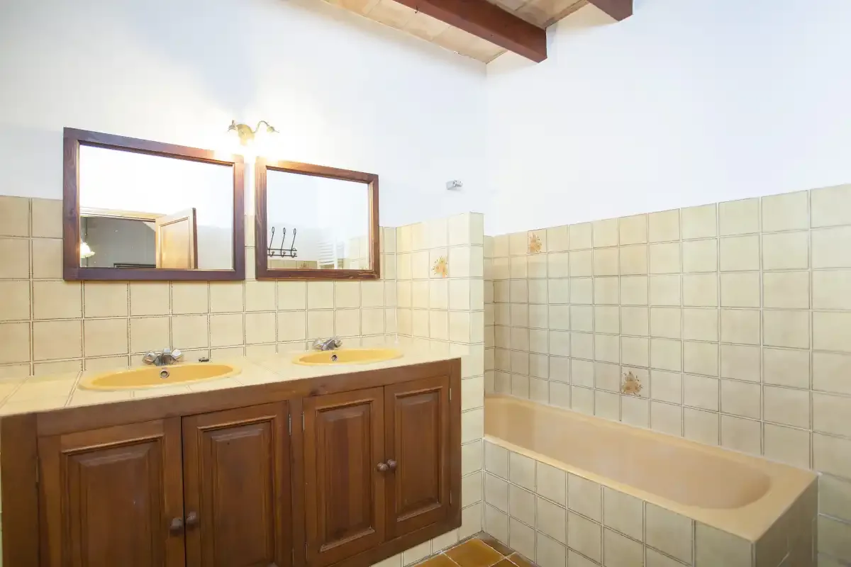 A tiled bathroom with a wooden vanity, two sinks, and a bathtub.