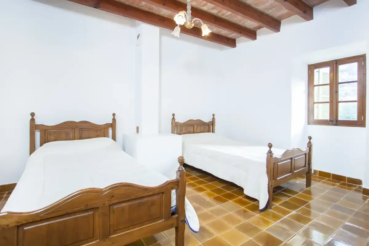 A bedroom with two wooden beds, white bedding, and a window.