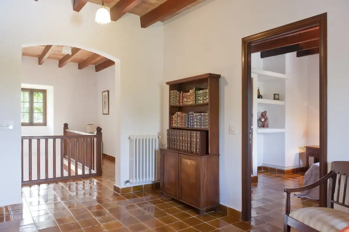 A tiled interior hallway with a wooden bookcase and open doorways.