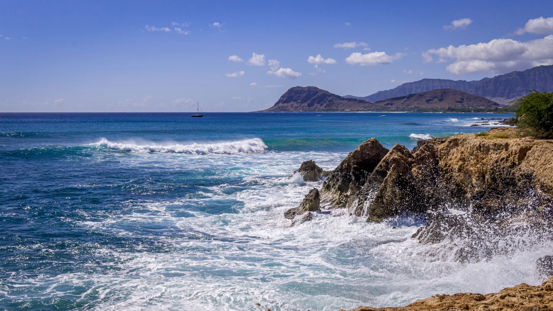 Las olas rompen contra una costa rocosa, con montañas visibles a lo lejos.
