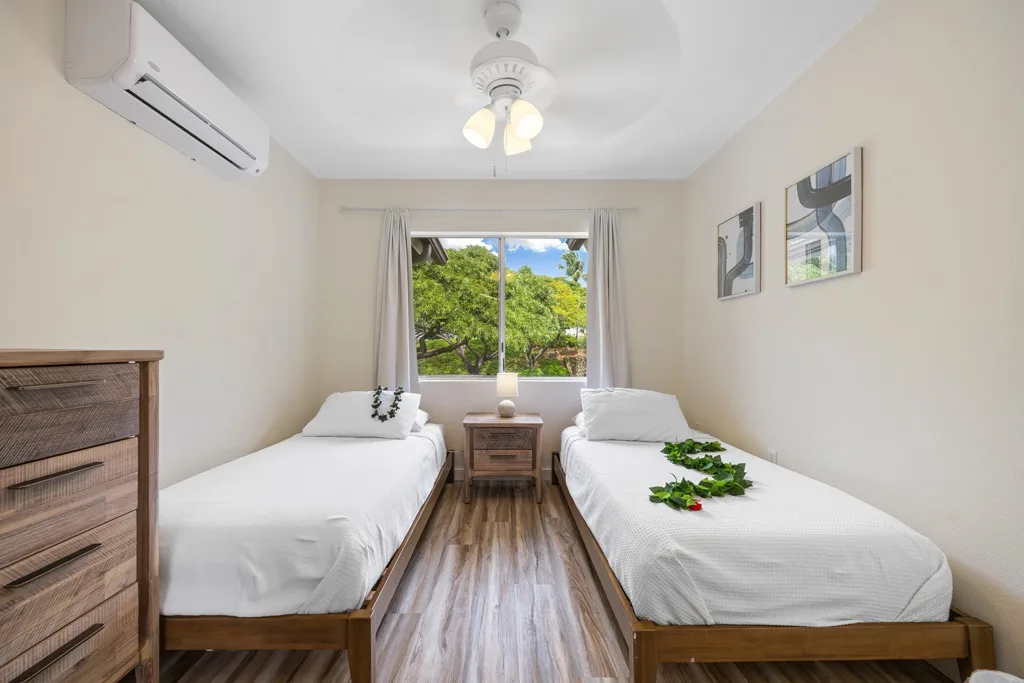 Un dormitorio luminoso con dos camas, una ventana y un ventilador de techo.