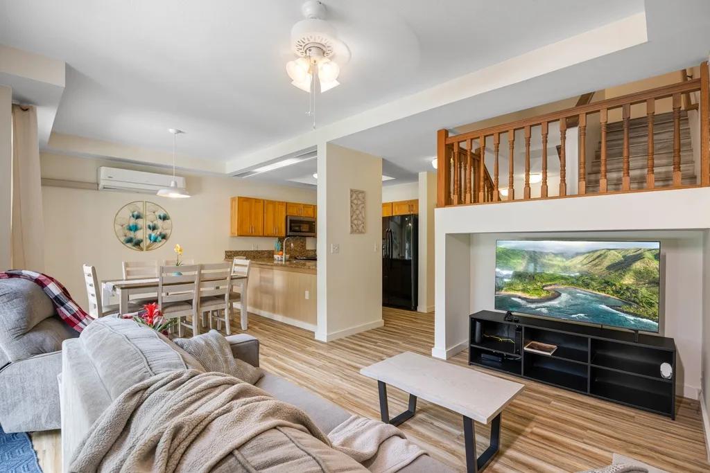 Una sala de estar se abre a un comedor y una cocina, con un televisor sobre un mueble bajo.